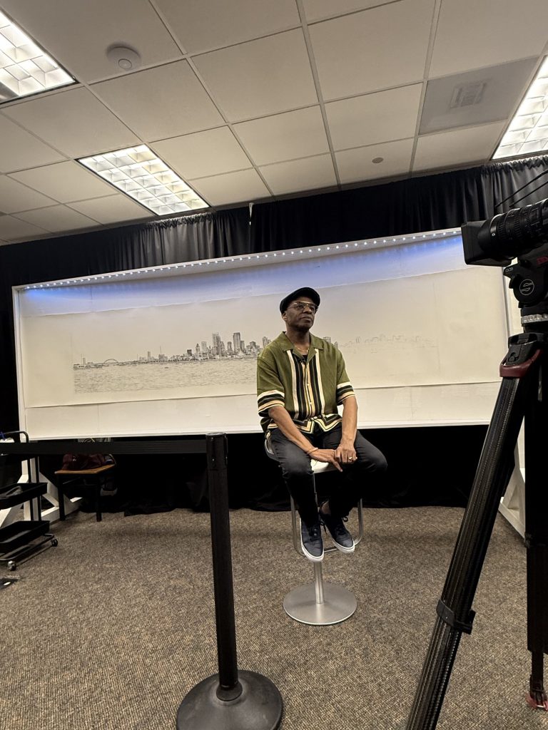 Stephen Wiltshire seated in front of his completed Milwaukee skyline panorama during filming